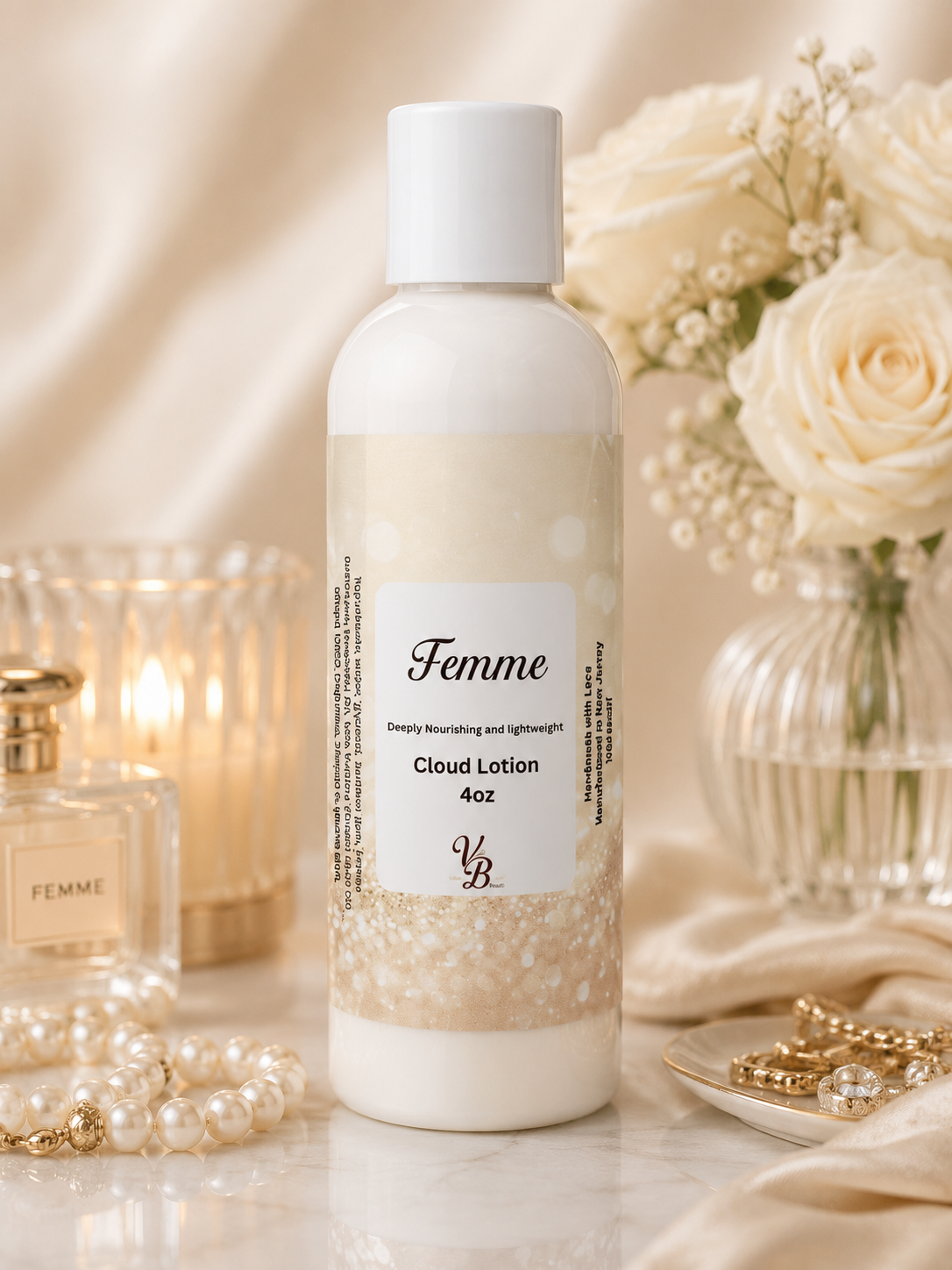 A bottle of Femme Cloud Lotion 4oz centered on a marble surface, surrounded by soft cream satin fabric, white roses in a glass vase, pearl strands, a lit candle, and gold jewelry. The product bottle is white with a beige-and-white label and a white cap.
